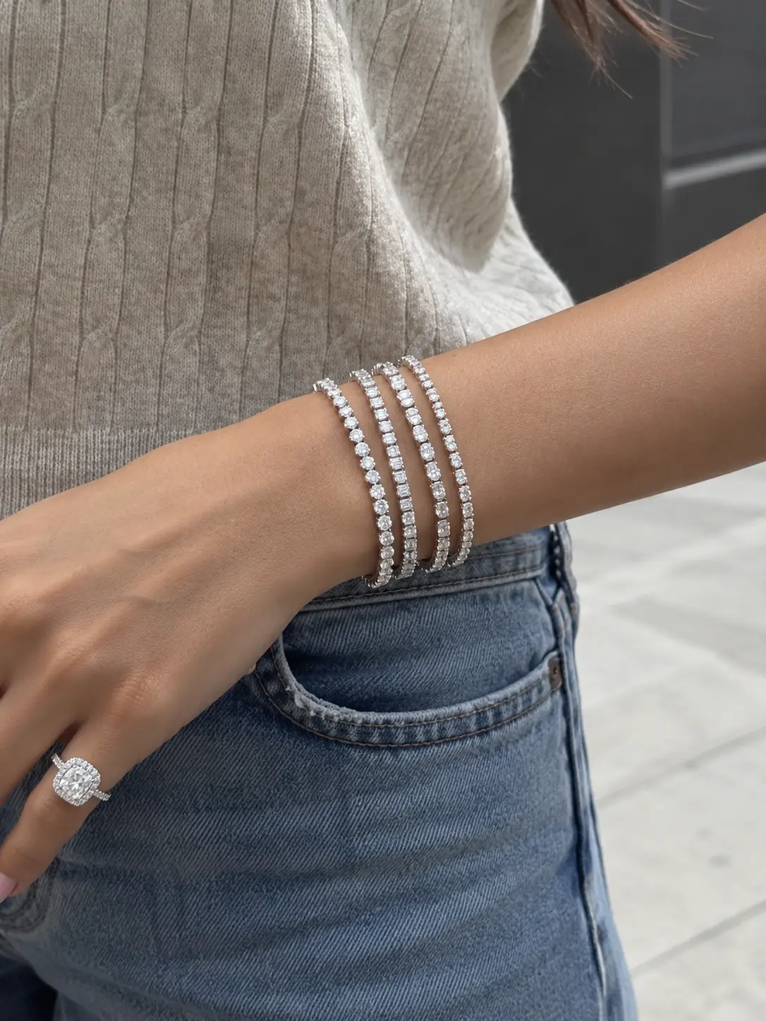 A model wearing a four-row diamond tennis bracelet stack and cushion halo ring against blue denim.